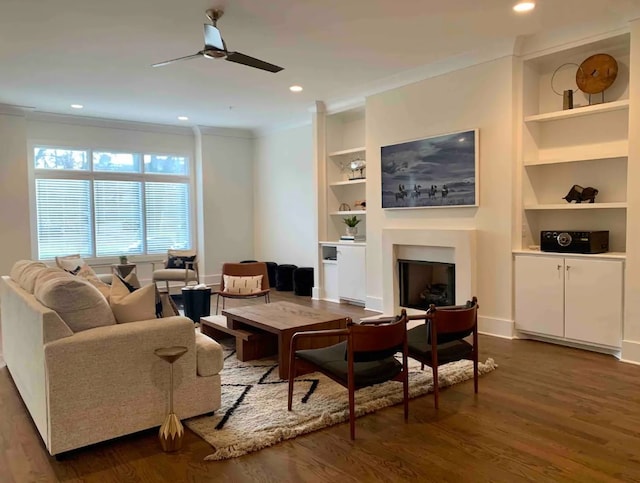 living room featuring built in features, ceiling fan, crown molding, and dark hardwood / wood-style floors