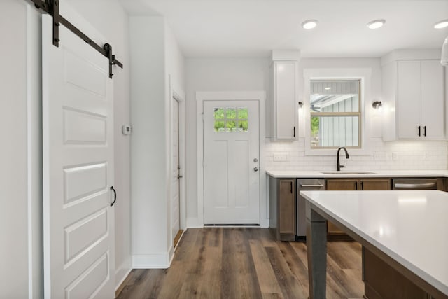 kitchen with dark hardwood / wood-style floors, white cabinetry, a barn door, dishwasher, and sink