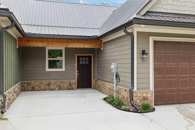 property entrance with stone siding, covered porch, metal roof, and an attached garage