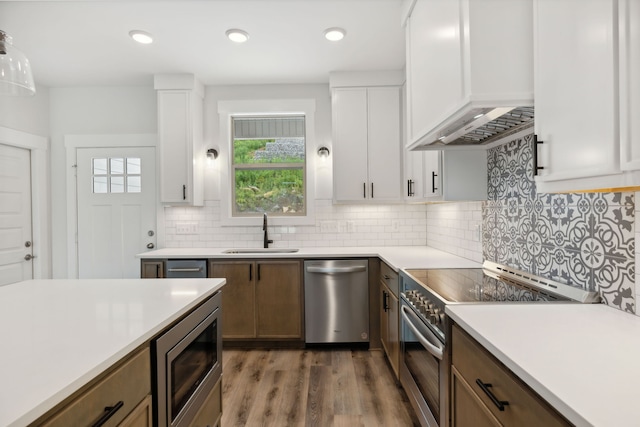 kitchen featuring appliances with stainless steel finishes, premium range hood, white cabinets, wood-type flooring, and sink