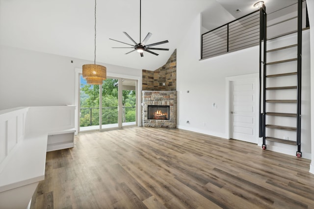 unfurnished living room with ceiling fan, a stone fireplace, dark wood-type flooring, high vaulted ceiling, and brick wall