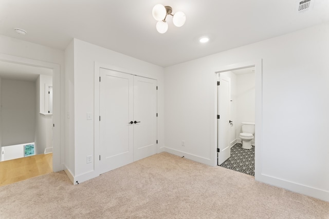 unfurnished bedroom featuring a notable chandelier, dark colored carpet, and ensuite bath