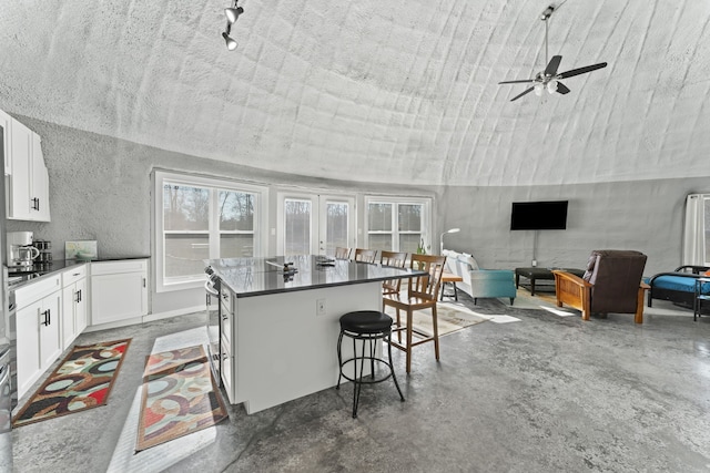 kitchen with ceiling fan, a breakfast bar, white cabinets, a center island with sink, and a textured ceiling