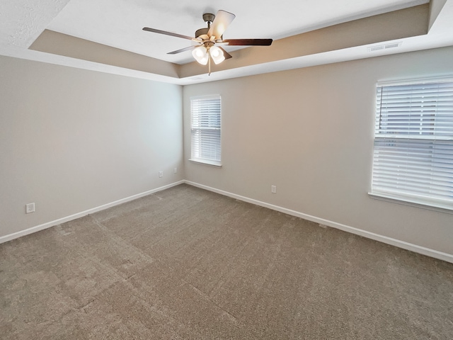 unfurnished room with a healthy amount of sunlight, a tray ceiling, ceiling fan, and carpet floors