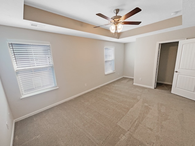 unfurnished bedroom with ceiling fan, a tray ceiling, light colored carpet, and a closet