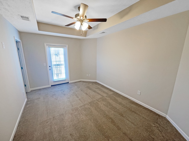 empty room featuring a raised ceiling, light carpet, and ceiling fan