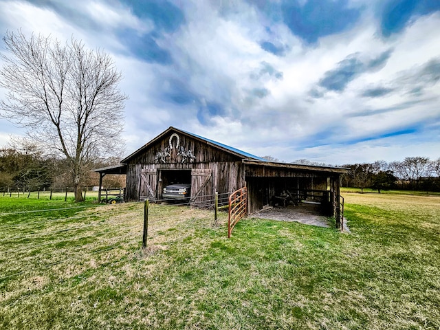 rear view of property featuring an outdoor structure, a lawn, and a rural view