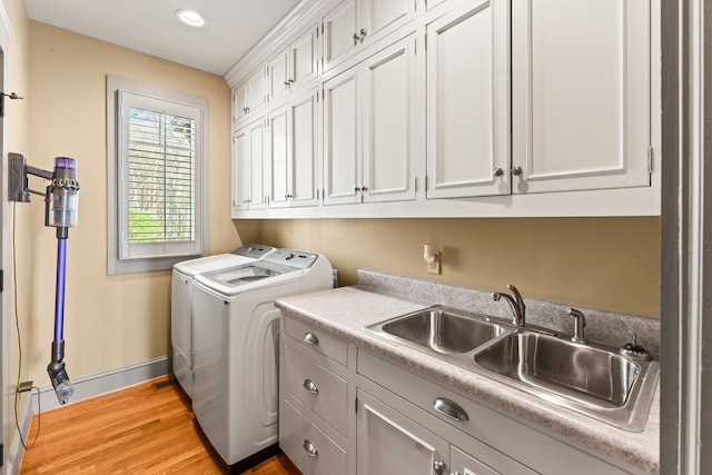 clothes washing area featuring cabinets, sink, light wood-type flooring, and washing machine and dryer