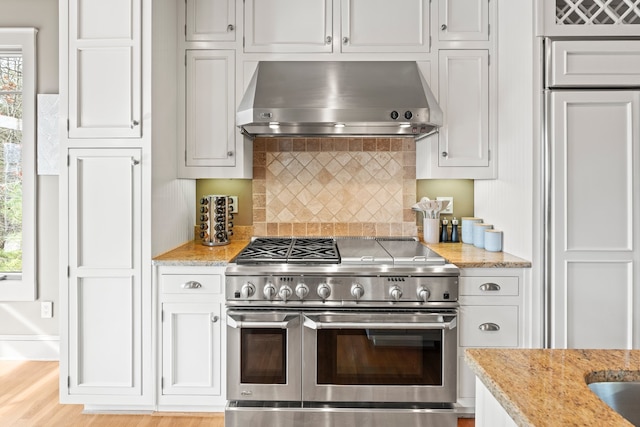 kitchen featuring range with two ovens, light hardwood / wood-style flooring, plenty of natural light, and wall chimney range hood