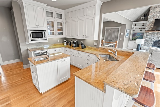 kitchen featuring a kitchen island with sink, stainless steel microwave, sink, and light hardwood / wood-style floors