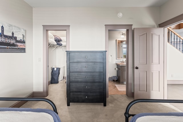 tiled bedroom with a walk in closet, ensuite bathroom, sink, and a closet