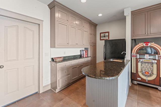 kitchen with black refrigerator, sink, tile patterned floors, and dark stone counters