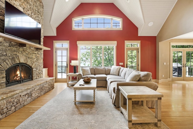 living room featuring french doors, high vaulted ceiling, light hardwood / wood-style flooring, and a stone fireplace