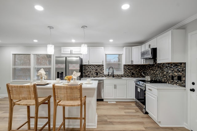 kitchen featuring appliances with stainless steel finishes, tasteful backsplash, white cabinetry, light hardwood / wood-style flooring, and hanging light fixtures