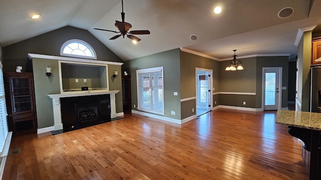 unfurnished living room with hardwood / wood-style flooring, vaulted ceiling, ceiling fan with notable chandelier, and ornamental molding