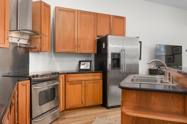 kitchen with appliances with stainless steel finishes, light hardwood / wood-style floors, dark stone countertops, wall chimney range hood, and sink