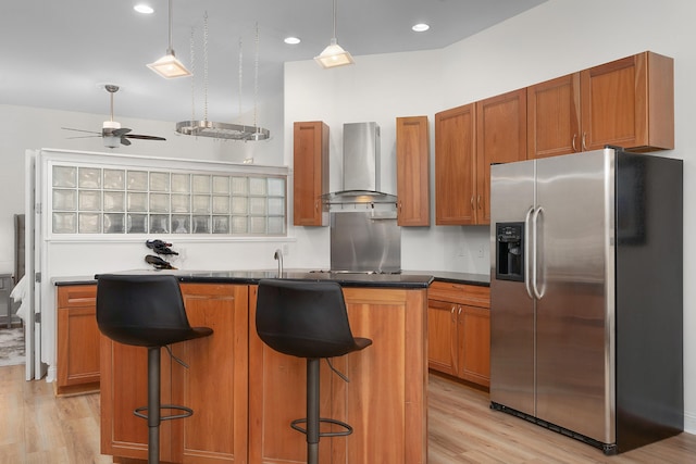 kitchen with stainless steel fridge with ice dispenser, light hardwood / wood-style floors, a center island, and wall chimney exhaust hood