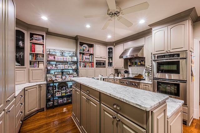 kitchen featuring ceiling fan, dark hardwood / wood-style flooring, appliances with stainless steel finishes, a center island with sink, and wall chimney range hood