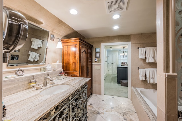 bathroom with tile walls, a relaxing tiled bath, vanity with extensive cabinet space, tile floors, and an inviting chandelier