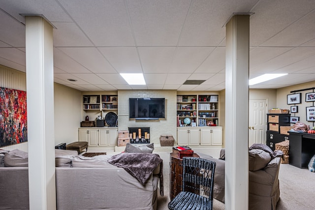 living room with a paneled ceiling, carpet, a brick fireplace, and built in shelves