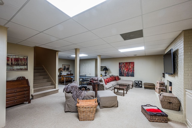 carpeted living room featuring brick wall and a drop ceiling