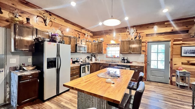 kitchen featuring pendant lighting, sink, light hardwood / wood-style flooring, stainless steel appliances, and wooden walls