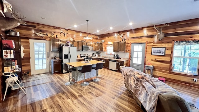 kitchen with a kitchen island, wooden walls, stainless steel appliances, a breakfast bar, and light wood-type flooring