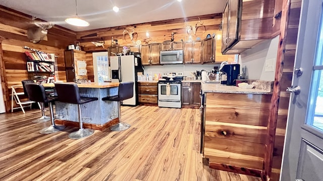 kitchen with hanging light fixtures, light hardwood / wood-style floors, white appliances, wood walls, and a kitchen bar