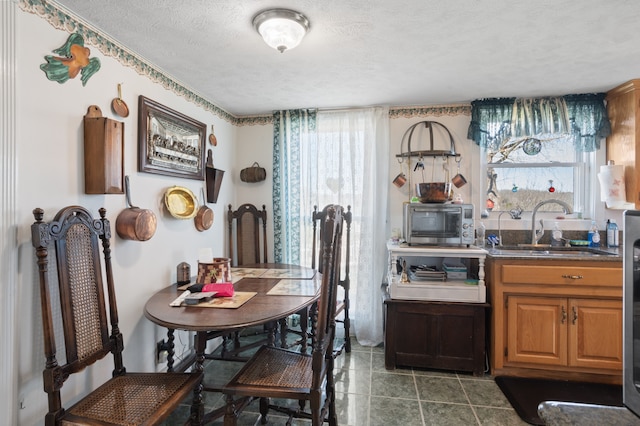 dining area with dark tile floors, a textured ceiling, sink, and a healthy amount of sunlight