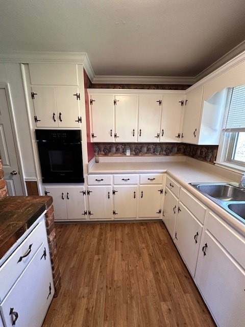 kitchen featuring dark hardwood / wood-style floors, crown molding, white cabinetry, and black oven