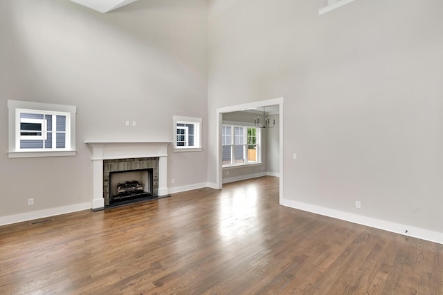 unfurnished living room featuring a high ceiling, a chandelier, hardwood / wood-style floors, and a fireplace