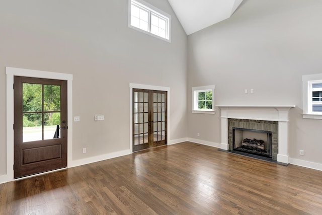 unfurnished living room featuring high vaulted ceiling, a tile fireplace, plenty of natural light, and dark hardwood / wood-style floors