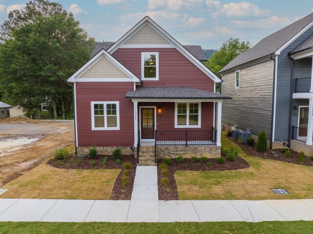 craftsman-style house with central air condition unit, a balcony, a front yard, and covered porch