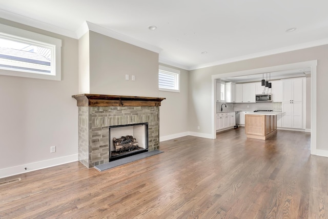 unfurnished living room featuring light wood-style floors, visible vents, a fireplace with raised hearth, and ornamental molding