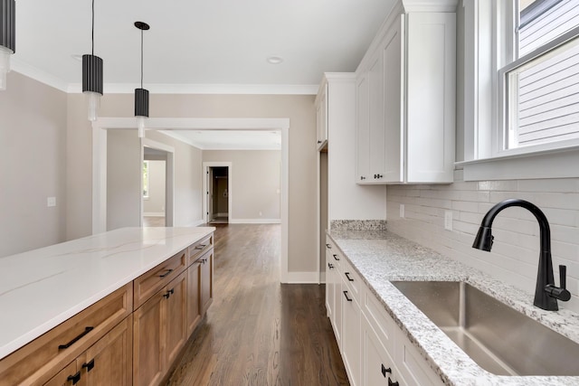 kitchen with light stone countertops, white cabinetry, a sink, and ornamental molding