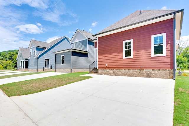 view of side of property with a shingled roof, concrete driveway, and a lawn