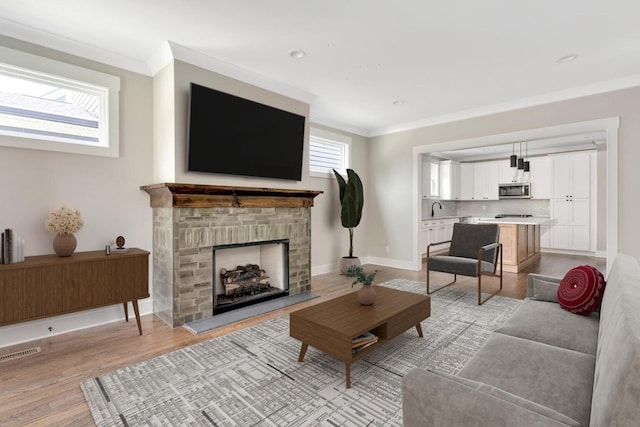 living room with ornamental molding, light wood-style flooring, visible vents, and baseboards