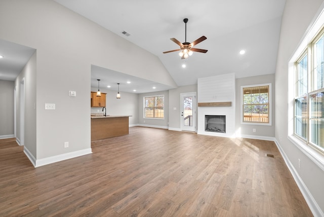 unfurnished living room featuring high vaulted ceiling, a large fireplace, dark hardwood / wood-style flooring, and a wealth of natural light