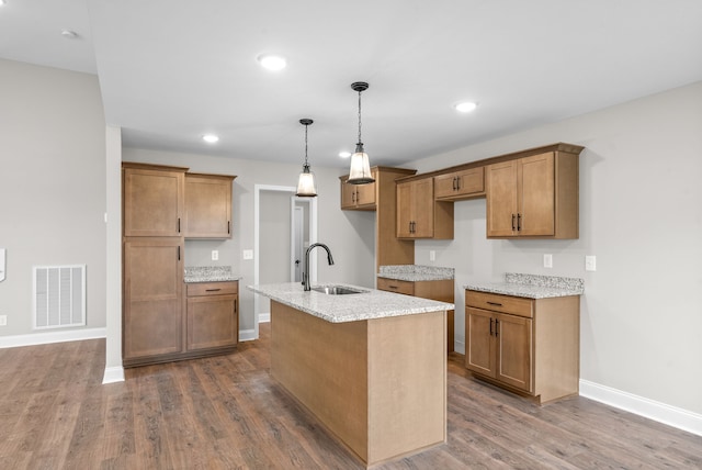 kitchen with light stone countertops, sink, hardwood / wood-style floors, decorative light fixtures, and a center island with sink