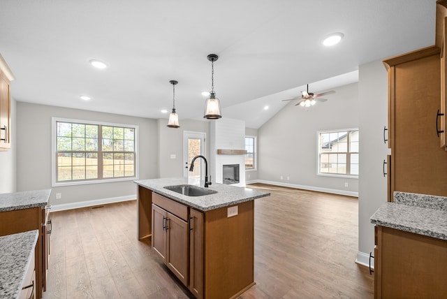 kitchen featuring pendant lighting, lofted ceiling, sink, an island with sink, and light hardwood / wood-style floors