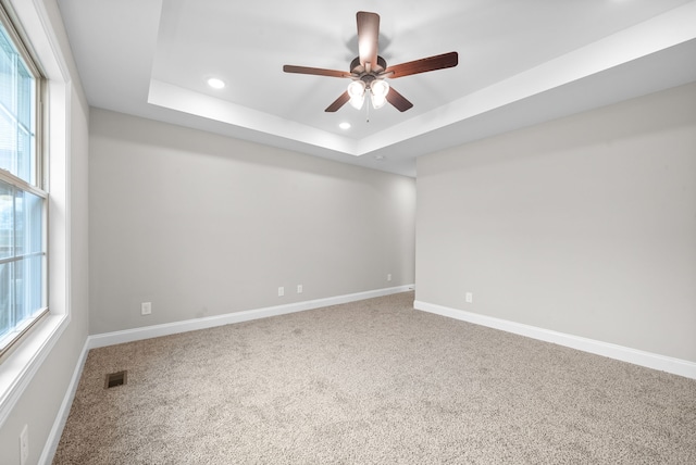 carpeted empty room with a raised ceiling and ceiling fan