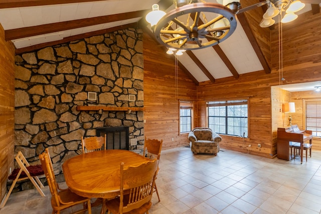 tiled dining area with beam ceiling, ceiling fan, high vaulted ceiling, wood walls, and a fireplace