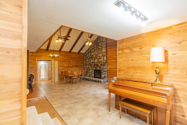 living room featuring wooden walls, lofted ceiling with beams, a textured ceiling, a fireplace, and ceiling fan