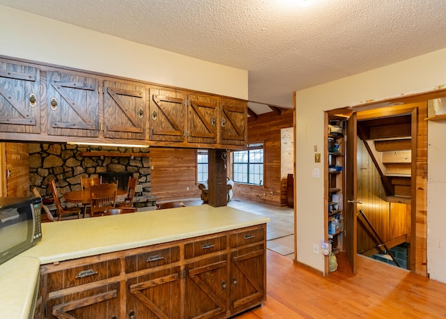 kitchen featuring a fireplace, a textured ceiling, wooden walls, and light wood-type flooring