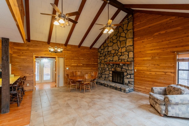 living room with a fireplace, ceiling fan, beamed ceiling, wooden walls, and high vaulted ceiling