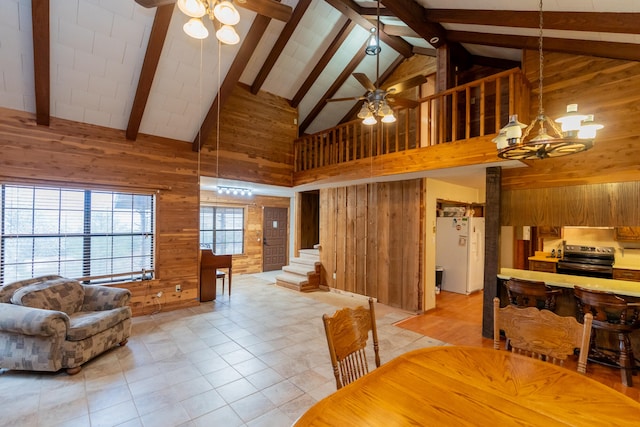 living room featuring wooden walls, ceiling fan with notable chandelier, and high vaulted ceiling