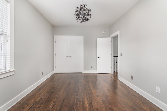 unfurnished bedroom with a closet, dark wood-type flooring, and an inviting chandelier