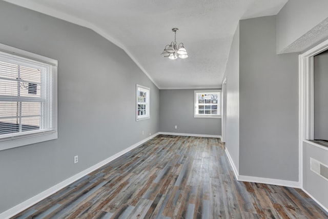 empty room with an inviting chandelier, dark hardwood / wood-style flooring, a textured ceiling, and vaulted ceiling