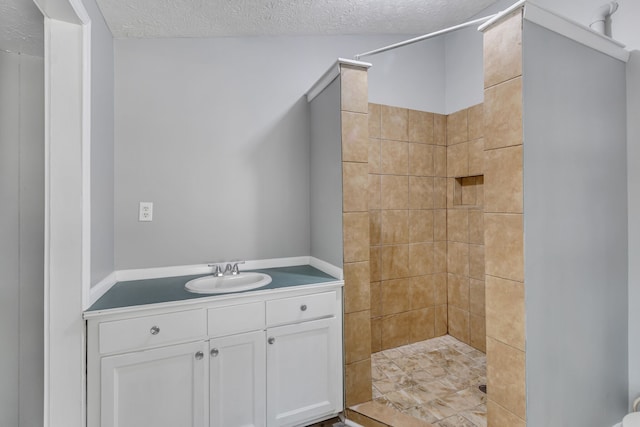 bathroom with a textured ceiling, a tile shower, and vanity