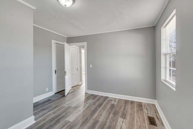 spare room with crown molding, light hardwood / wood-style flooring, a textured ceiling, and a healthy amount of sunlight